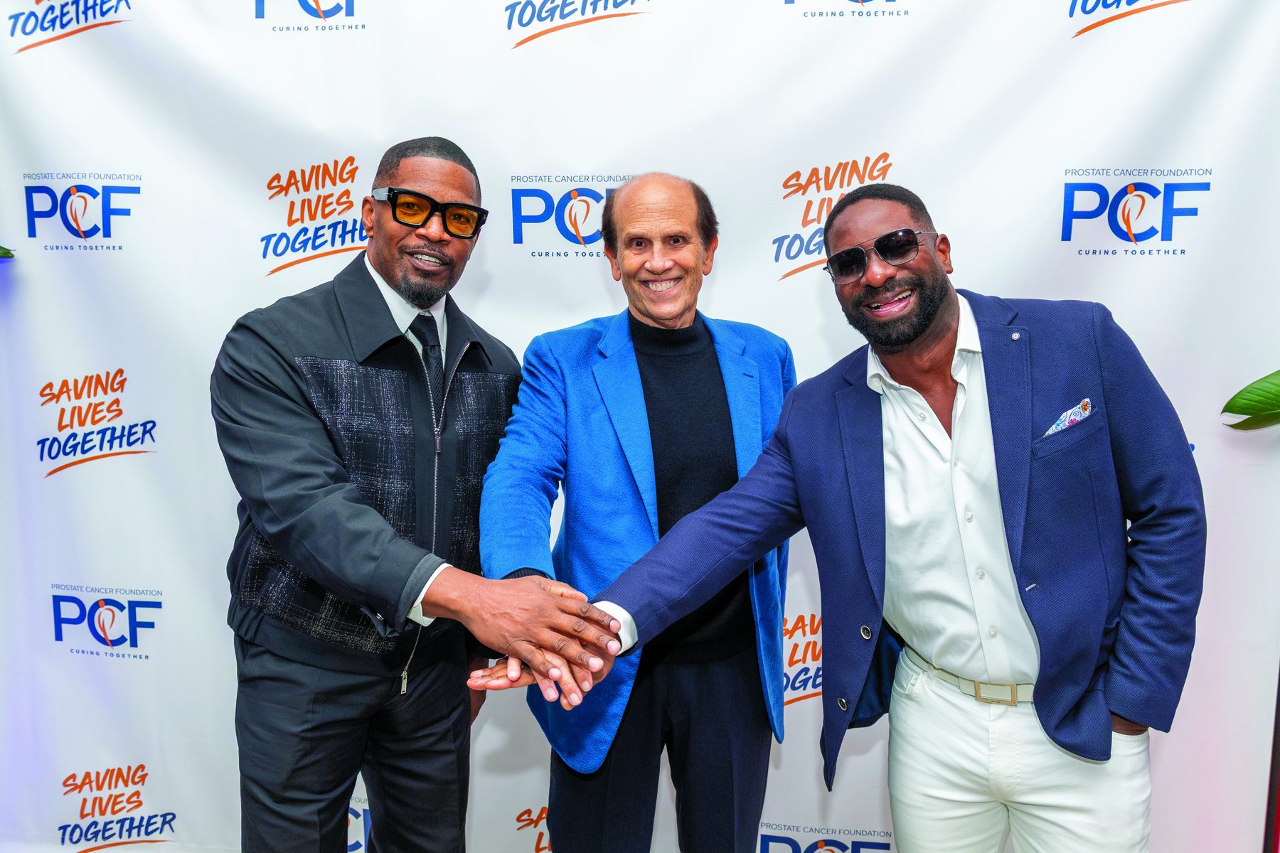 Guests photographed in front of a step-and-repeat backdrop carrying the PCF mark and the Saving Lives Together event brand.